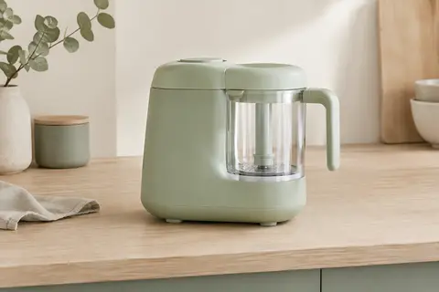Robot cuiseur bébé vert clair avec récipient en Tritan, posé sur un plan de travail en bois clair.