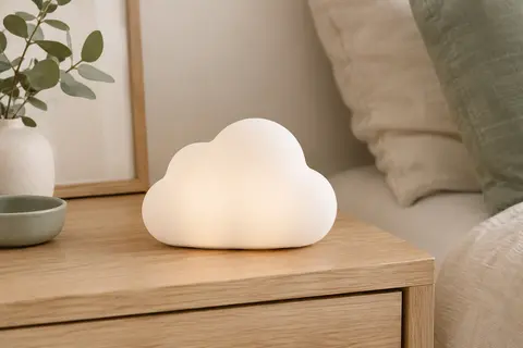 Veilleuse blanche en silicone souple en forme de nuage, posée sur une table de chevet en bois clair.