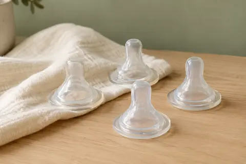 Lot de quatre tétines plates transparentes en silicone, disposées sur du bois clair avec un linge ivoire