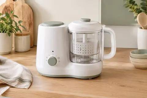 Robot cuiseur bébé blanc avec panier vapeur, posé sur un plan de travail en bois clair
