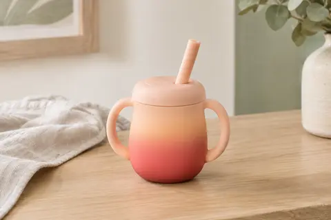 Tasse bébé en silicone avec poignée et paille souple, posée sur une surface en bois clair