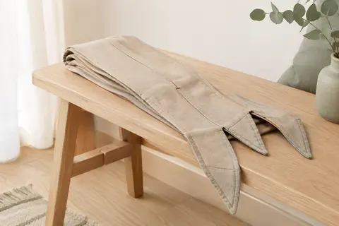 Écharpe de portage Laleni en coton beige pliée sur un banc en bois clair