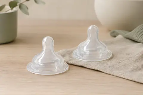 Deux tétines de biberon en silicone transparent posées sur un fond ivoire et sauge.
