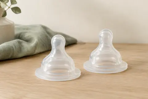 Deux tétines transparentes NUK First Choice+ Flow Control en silicone présentées sur une surface en bois clair.