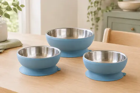 Trois bols pour bébé en acier inoxydable avec base à ventouse en silicone bleu, posés sur une table claire.