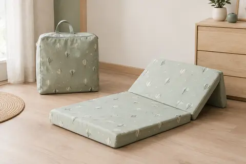 Matelas bébé pliant vert à motif de ballons, présenté avec son sac de transport dans une chambre claire.