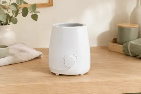 Chauffe-biberon électrique blanc Tommee Tippee avec commande à molette, posé sur un plan de travail en bois clair.