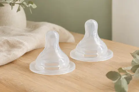 Deux tétines de biberon en silicone clair à débit rapide, posées sur un fond ivoire et sauge.
